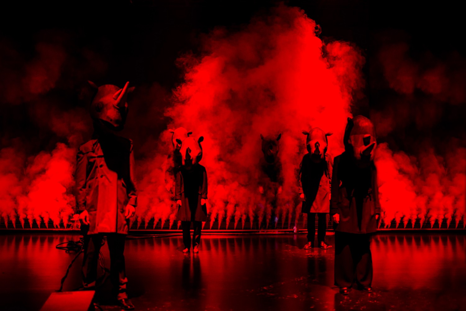 Actors with rhinoceros costumes standing on a stage filled with red light and smoke